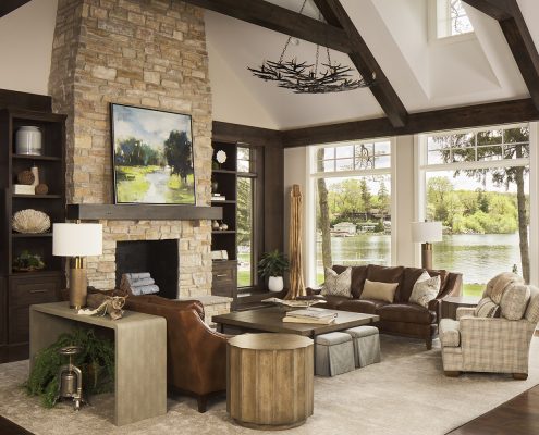 stone fireplace,. great room, leather sofas, cocktail table, side table, book cases, rug, console table, table lamp, arm chair, ottomans, pillows, accessories, lake view, chandelier