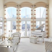 Tall arched windows with elegant drapery allow light to spill into a neutral color palette home with custom furnishings