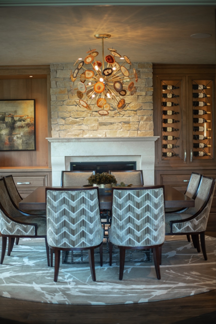 dining room, chevron pattern cahirs, stone fireplace, chandelier, wine cabinet, rug, square table, wall art
