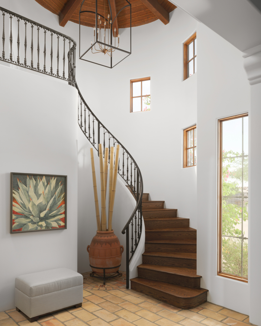 open-frame metal chandelier, Arizona two-story foyer, curved staircase, terra cotta floor, upholstered bench, decoratgive clay pot with tall branches