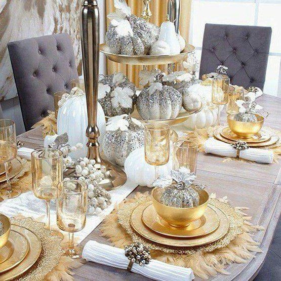 A tiered centerpiece stacked with glitter-encrusted miniature pumpkins mixes with glossy-white glass pears and squashes in varying sizes, radiating a festive Thanksgiving spirit.